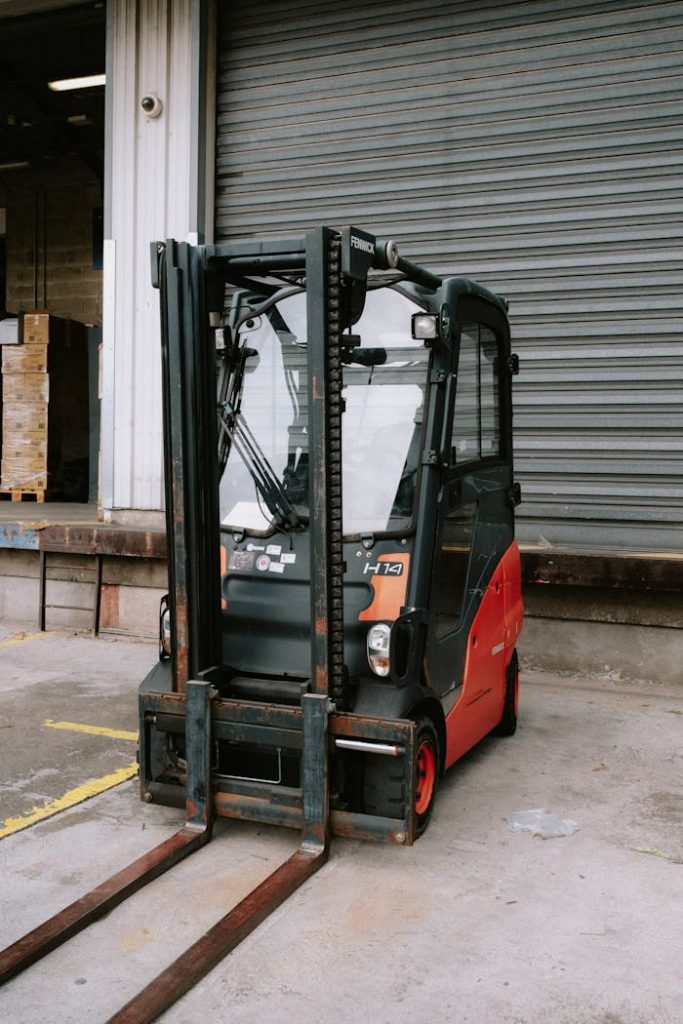 a-red-and-black-fork-lift-11666905 Close-up of a parked forklift in an industrial warehouse dock area.