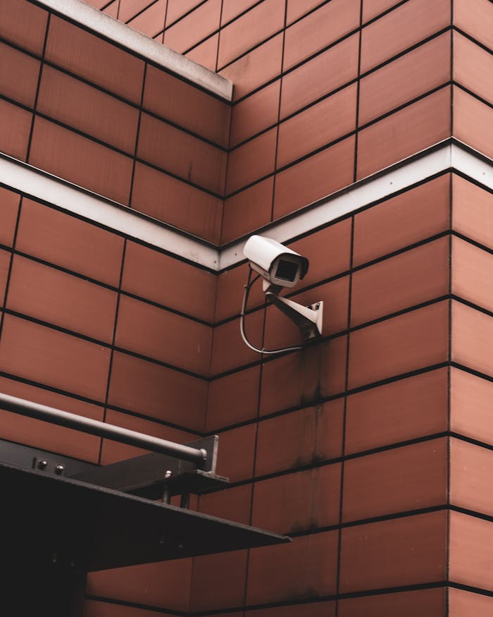 surveillance-camera-mounted-in-the-wall-5213883 Security camera monitoring a red brick building exterior, symbolizing modern surveillance in Germany.